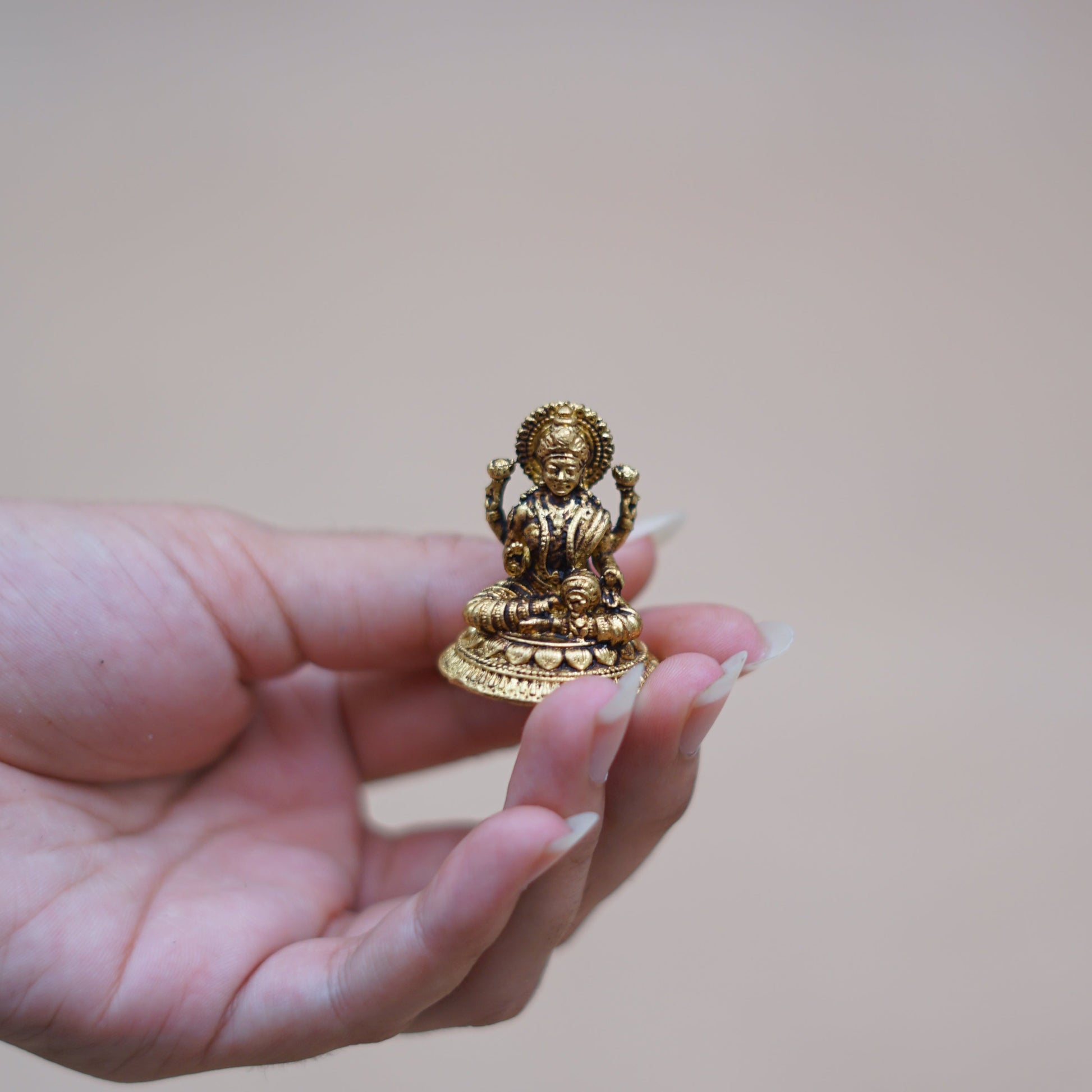 Hand holding a small brass statue of Goddess Lakshmi